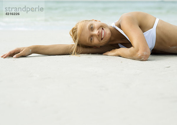 Frau am Strand liegend  lächelnd vor der Kamera