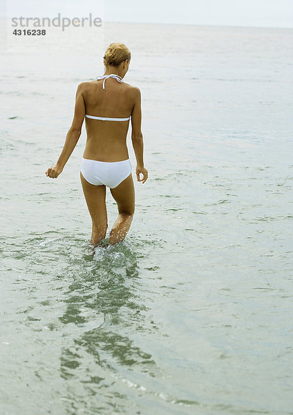 Frau im Bikini  knietief im Wasser  Rückansicht