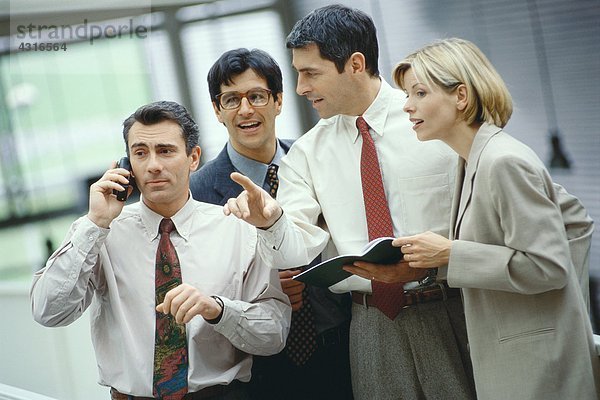 Vier Geschäftskollegen stehen in einer Gruppe  einer telefoniert  der andere hört zu.