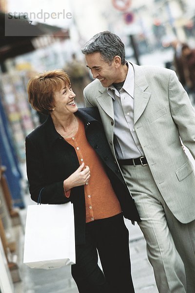 Ein reifes Paar  das auf dem Bürgersteig geht und sich gegenseitig anlächelt.