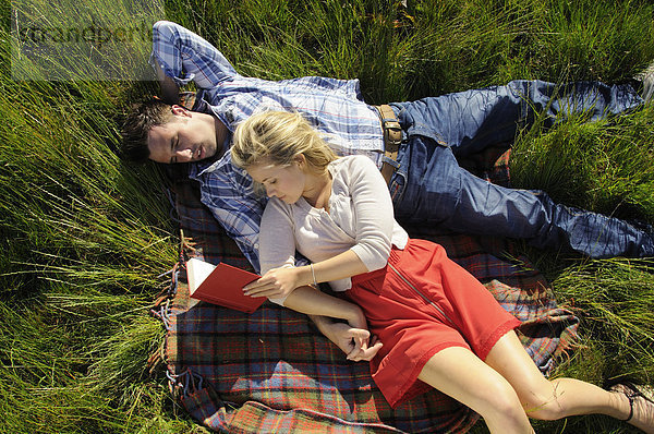 Paar liegt auf einer Decke und liest gemeinsam im Freien.
