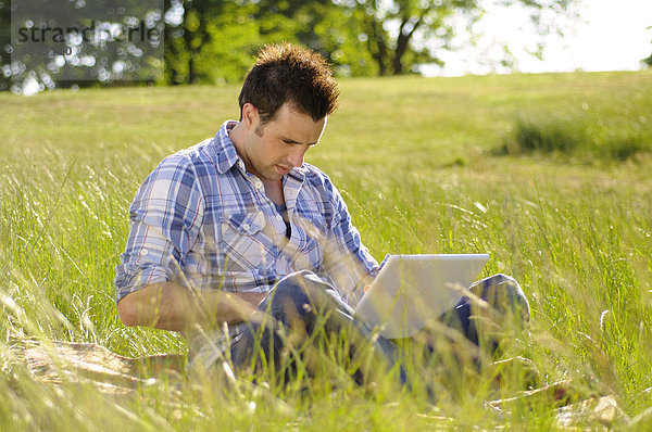 Junger Mann mit Laptop im Park