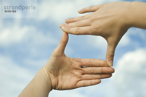 Hände machen einen Fingerrahmen vor dem Himmel