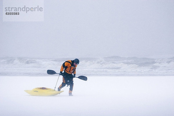 Winter Mann bedecken Strand Sturm ziehen Kajak Bucht Schnee Brandung