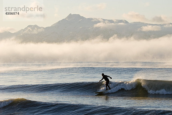 Mann Surfen im Moring in der Nähe von Homer Kachemak Bay w/Kenai Mountains Kenai-Halbinsel in Alaska Winter