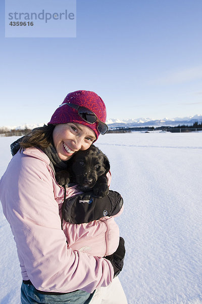 Junge Frau umarmt ihre Berner Sennenhund Welpen im Freien im Winter in der Nähe von Homer  Alaska