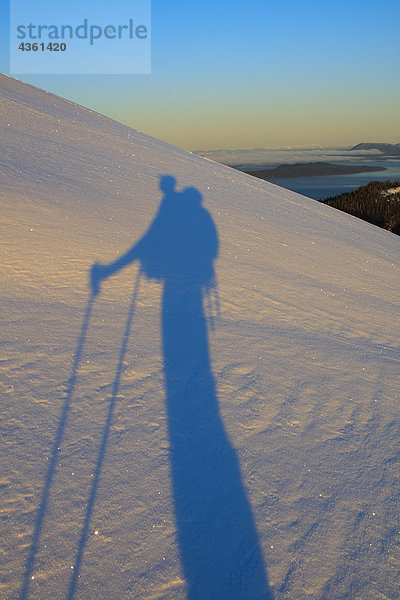 Ein Skifahrer wirft einen langen Schatten auf Schnee im Morgengrauen  wie er einen Berg auf Wrangell Island  Alaska steigt