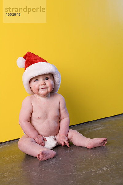 Helligkeit Portrait Winter sitzend Boden Fußboden Fußböden Wand gelb Hut frontal Windel Säuglingsalter Säugling Kleidung Mädchen
