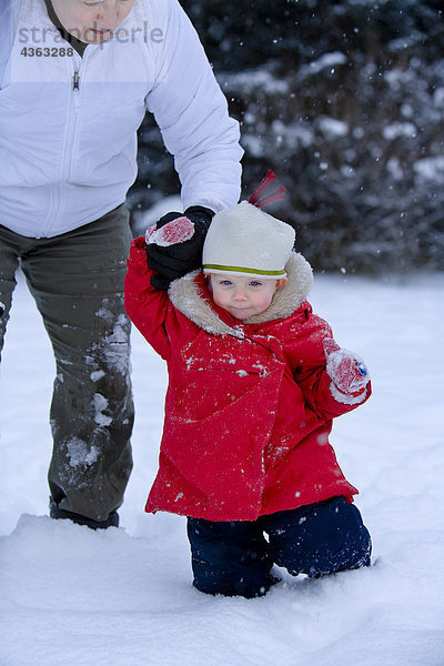 Mutter hält Hand ein Kleinkind Mädchen zu Fuß durch den Schnee im Winter in Anchorage  Alaska
