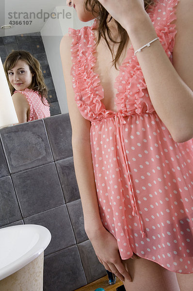 Junge Frau im Nachthemd vor dem Badezimmerspiegel