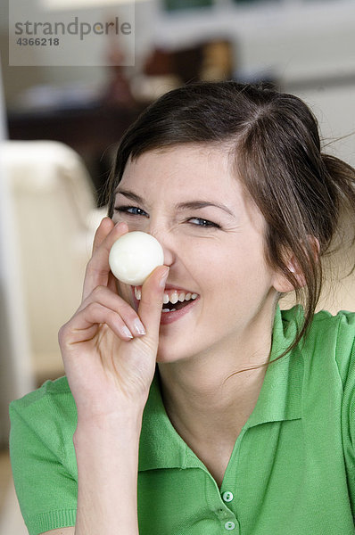 Junge lächelnde Frau bedeckt ihre Nase mit hart gekochtem Ei