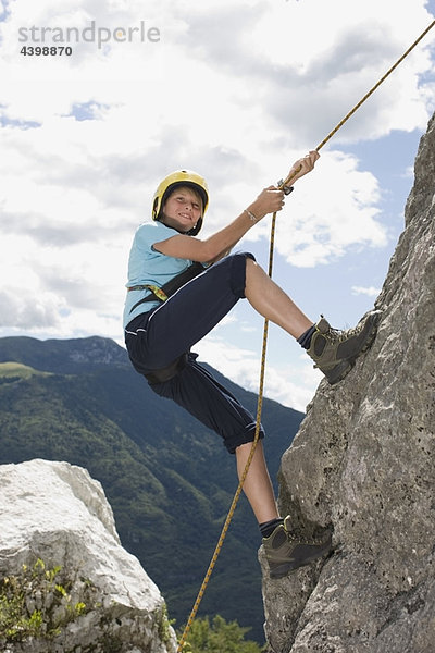 Junge klettert mit einem Seil auf einen Felsen