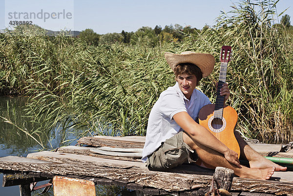 Mann am Steg mit Gitarre in der Sonne