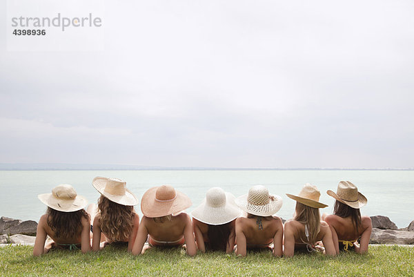 Frauen mit Strohhut liegen am See.