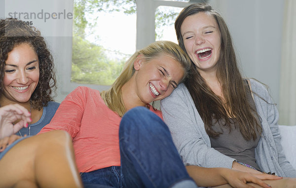 Junge Frauen lachen gemeinsam auf der Couch.