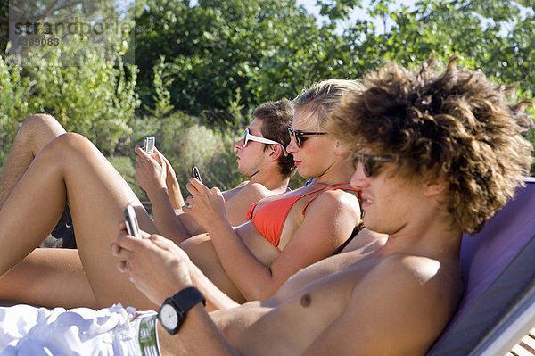 Teenager-Gruppen-Check-Telefone in der Sonne liegend