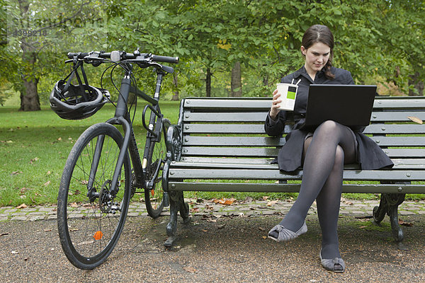 Frau schaut auf Laptop und isst Mittagessen