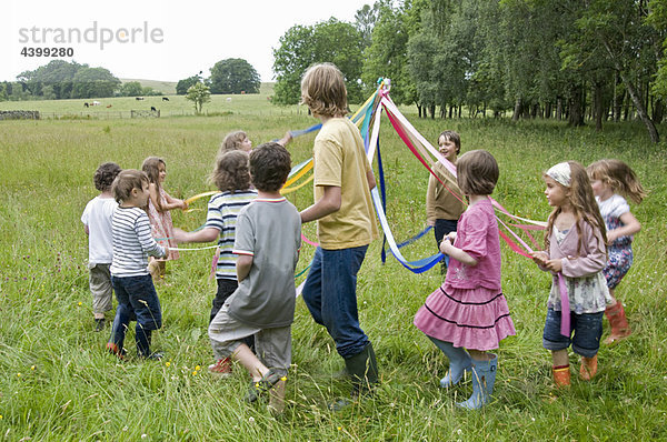 Kinder tanzen um Maibaum auf der Wiese