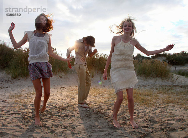 Freunde tanzen am Strand bei Sonnenuntergang