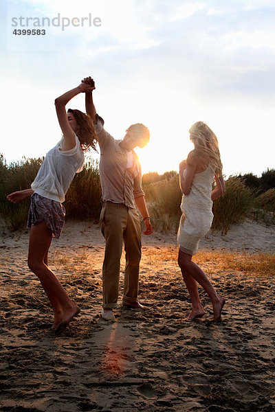 Freunde tanzen am Strand bei Sonnenuntergang