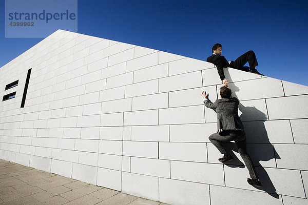 Mann hilft anderem Mann über die Mauer