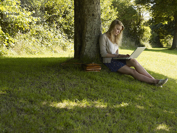 Mädchen auf einem Computer unter einem Baum