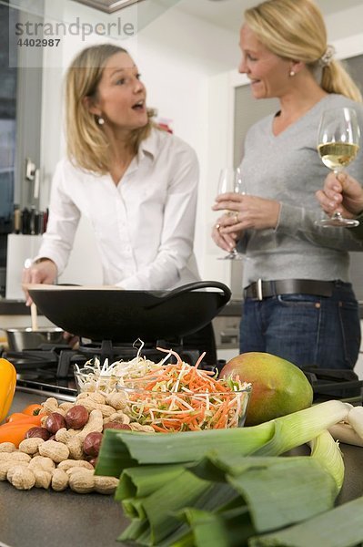 Frauen mit Gläser Wein chatten während der Vorbereitung Essen