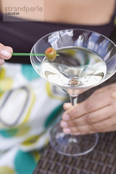 Frau hält grüne Olive auf cocktail-Stick über Martini-Glas