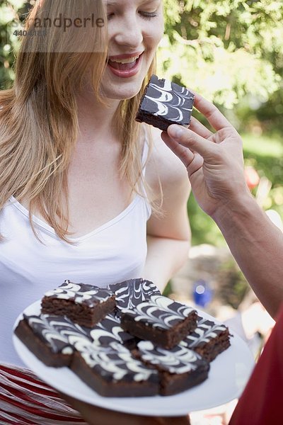 Mannes hand bietet Frau ein Brownie auf einer Gartenparty