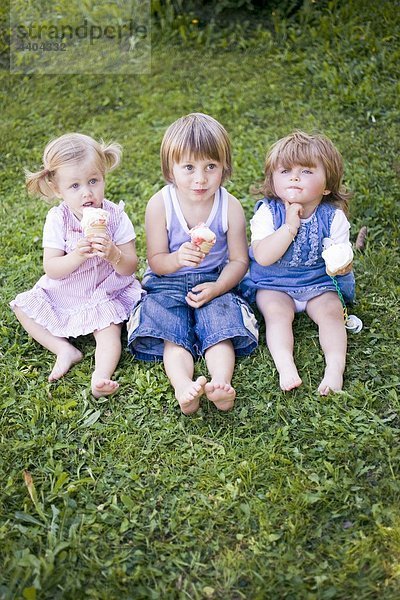 Drei Kinder mit Eiskrem sitzen auf Gras