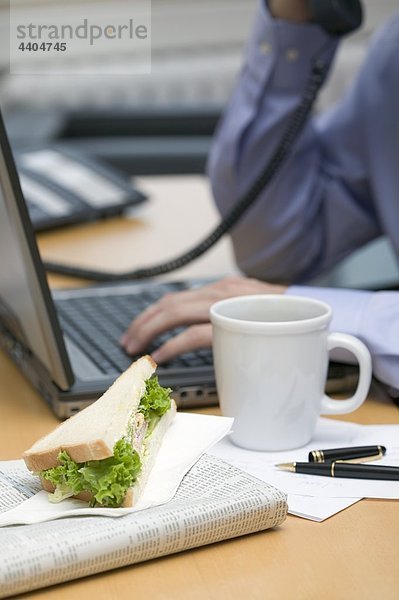 Kaufmann auf Telefon  Sandwich und Kaffee auf Schreibtisch