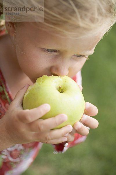 Kleine Mädchen essen einen großen grünen Apfel