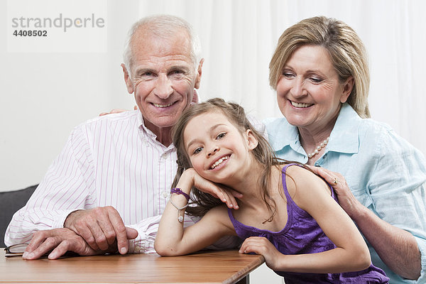 Enkelin (6-7) Kopf in Hand mit den Großeltern  lächelnd