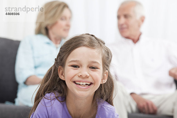 Enkelin (6-7) lächelnd mit Großeltern im Hintergrund
