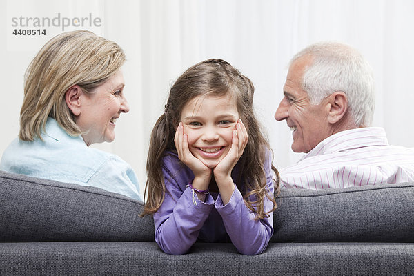 Enkelin (6-7) lächelnd mit Kopf in der Hand und Großeltern im Hintergrund