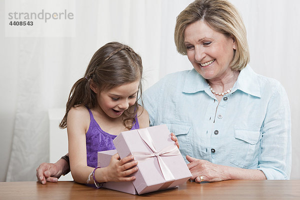 Enkelin (6-7) öffnet Geschenkbox und Großmutter lächelt