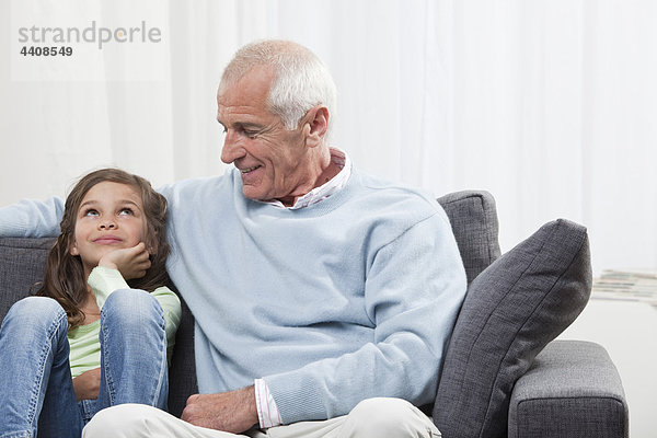 Enkelin (6-7) und Großvater auf der Couch sitzend  lächelnd