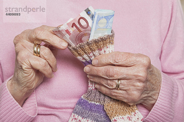 Deutschland  Seniorin beim Zählen von Geld aus Geldsocken  Mittelteil