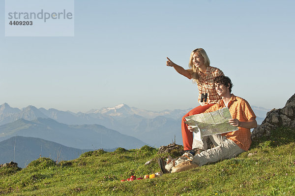 Junges Paar sitzt auf einem Berggipfel  Mann mit Karte  lächelnd.