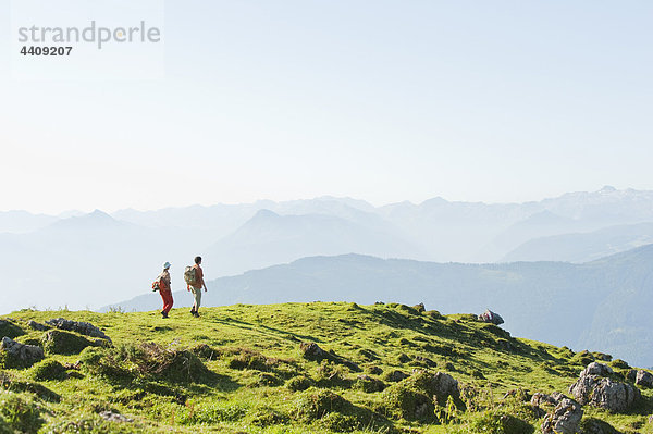Junges Paar steht auf einem Berggipfel und schaut auf die Aussicht.