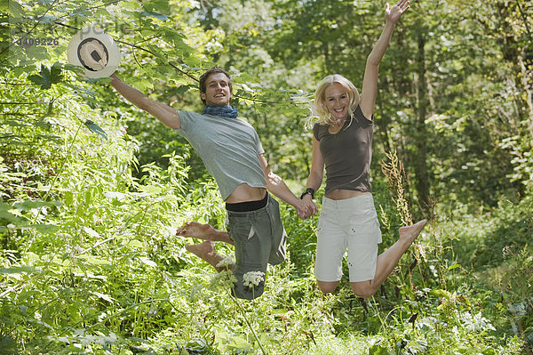 Junges Paar hält sich an den Händen und springt im Wald.