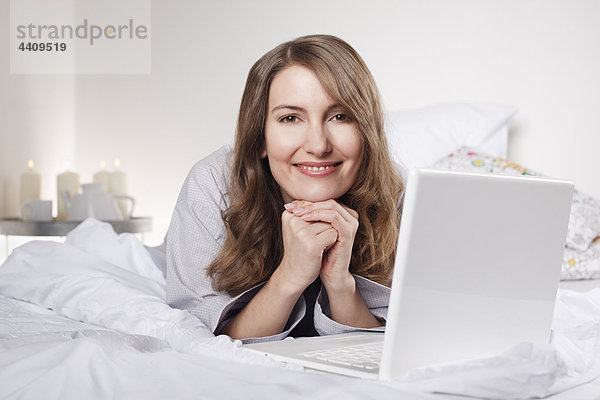 Frau auf dem Bett liegend mit Laptop  lächelnd  Portrait