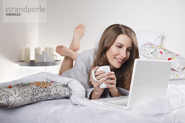 Frau auf dem Bett liegend mit Laptop  lächelnd