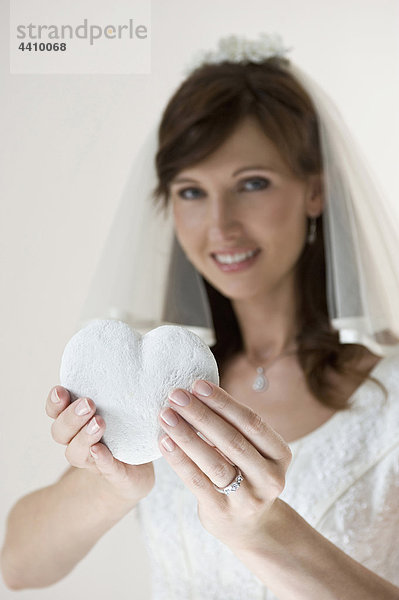 Porträt einer Braut mit herzförmigem Kopfkissen  lächelnd