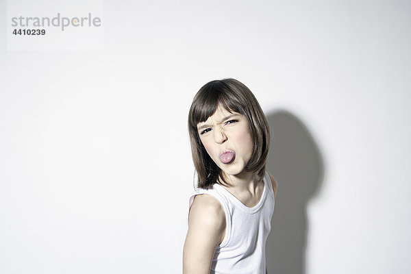 Mädchen (10-11) mit herausstehender Zunge vor weißem Hintergrund