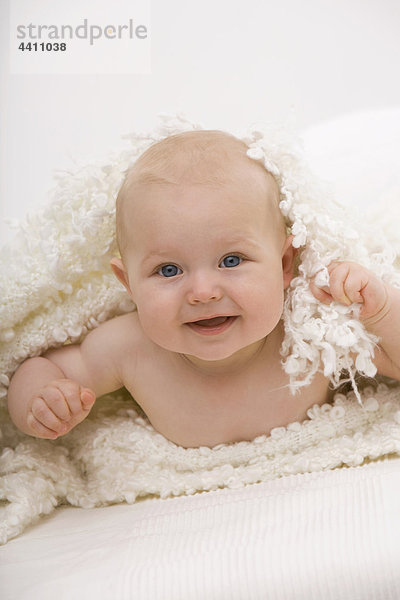 Junge (6-11 Monate) auf dem Bett liegend  lächelnd  Portrait