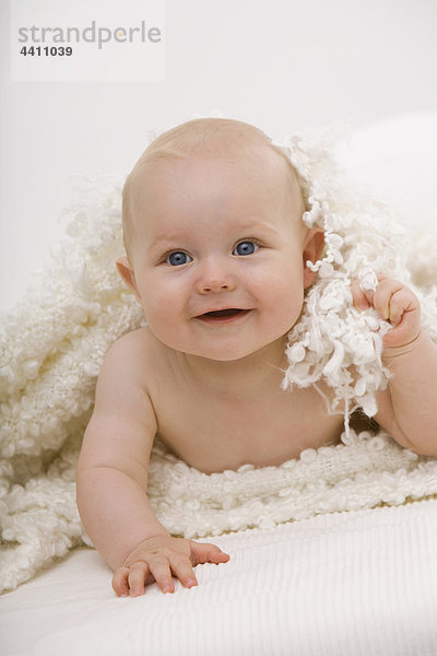 Junge (6-11 Monate) auf dem Bett liegend  lächelnd  wegschauend