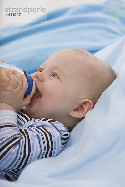 Babyboy (6-11 Monate) hält Babyflasche  schaut nach oben