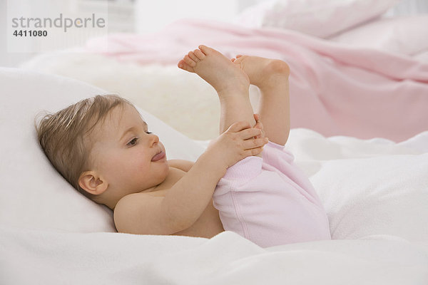 Kleines Mädchen (6-11 Monate) streckt die Zunge mit den Füßen nach oben.