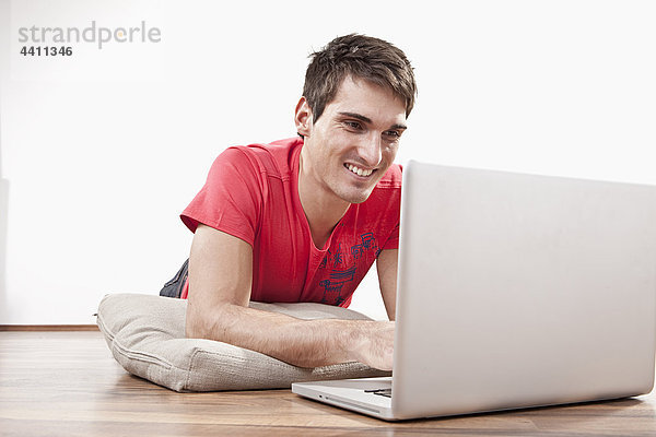Junger Mann auf dem Boden liegend mit Laptop  lächelnd